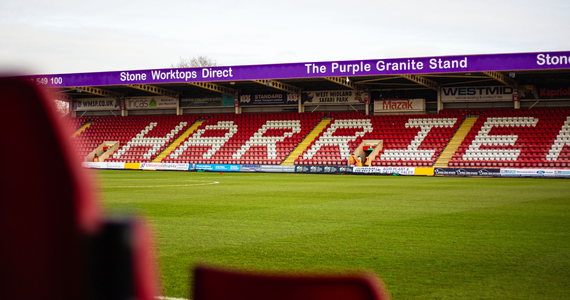 Inside of football stadium. Seating behind the picture spells Harriers in white seats.