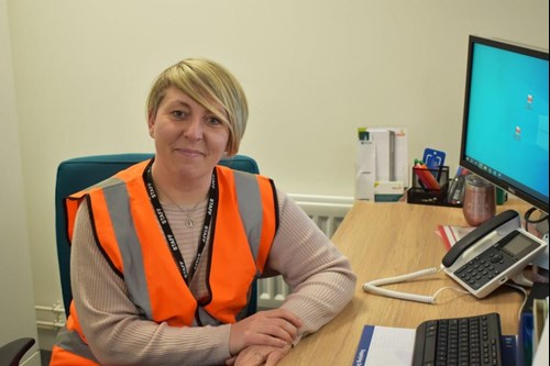 smiling woman in high vis vest sat at desk