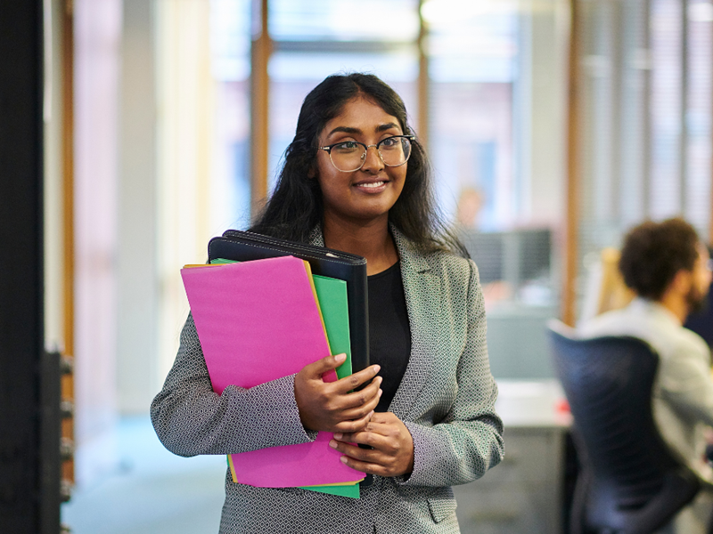 A young woman in an office holding colourful folders