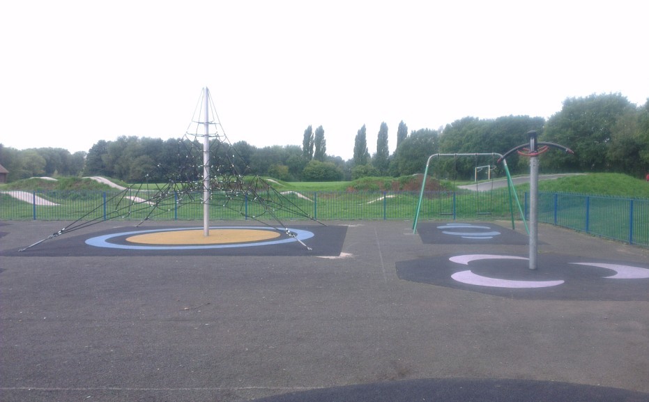 Older children's soft surface play area with climbing apparatus located within grassed area in public park.
