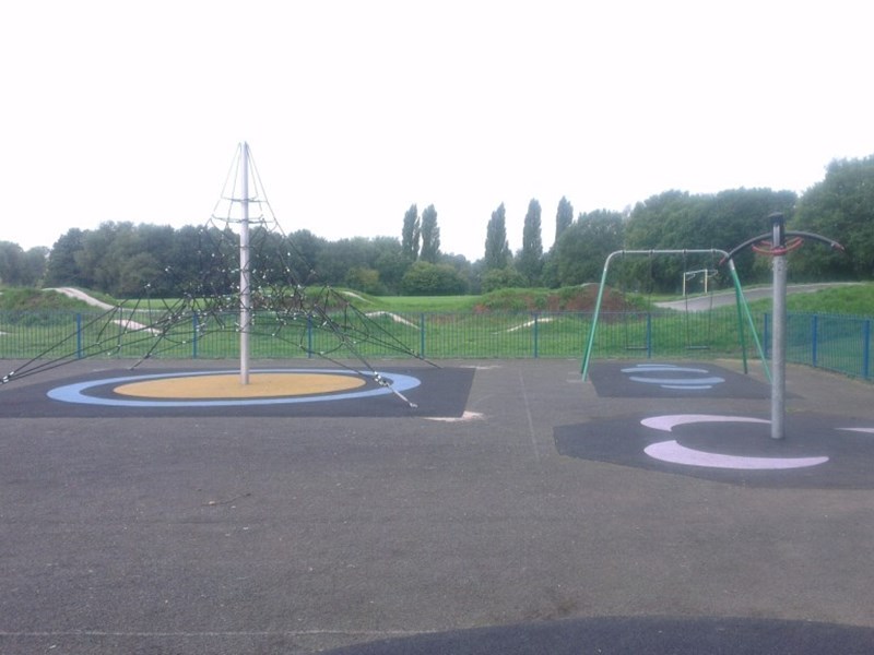 Older children's soft surface play area with climbing apparatus located within grassed area in public park.