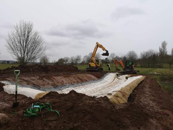 diggers in background behind large area of freshly dug soil