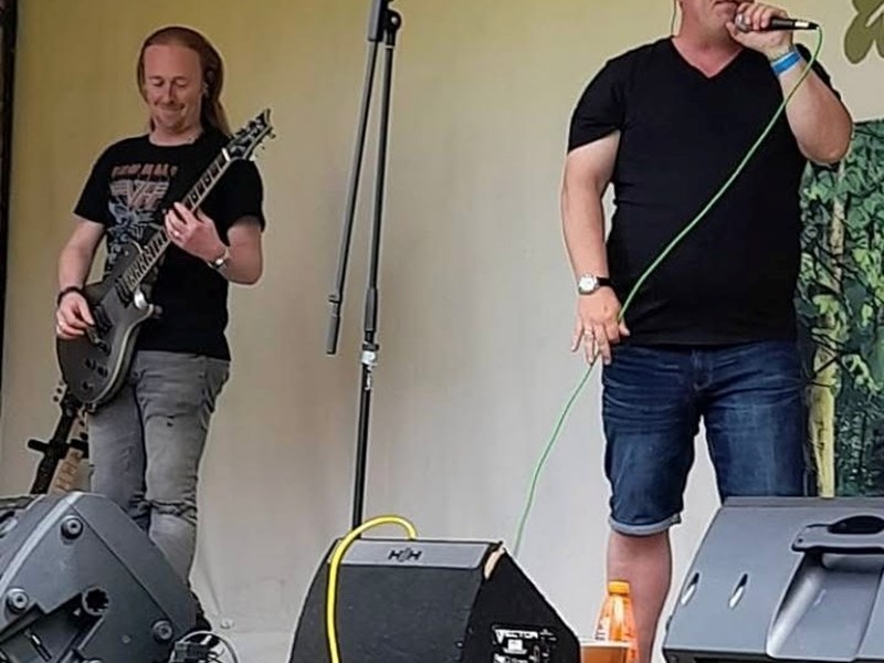 Photo of 2 male musicians on stage - one with a guitar and one singing with a microphone
