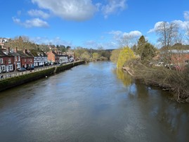 wide river with trees on right bank and buildings on left