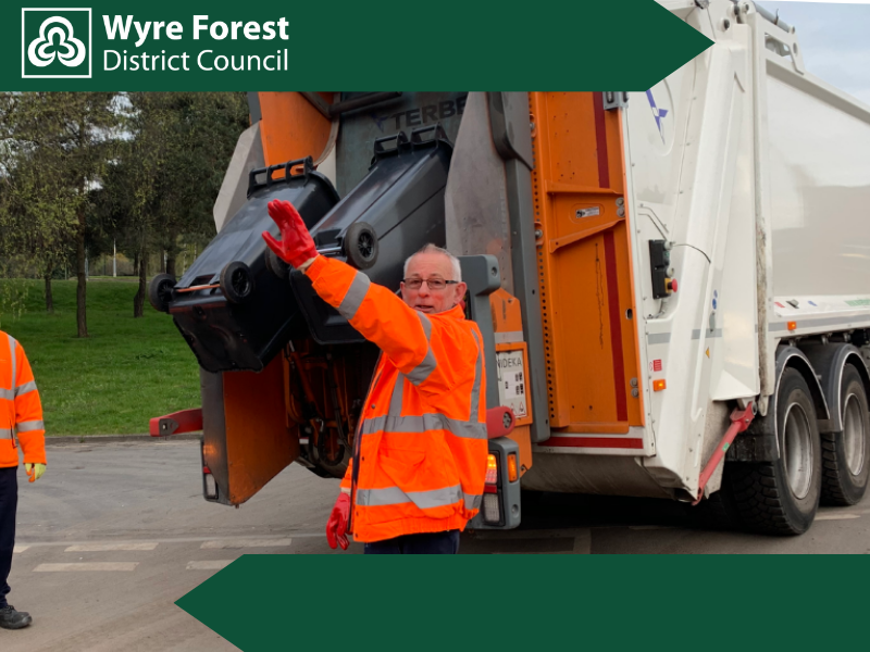 A man in an orange high vis outfit loading a black bin into a waste lorry. 